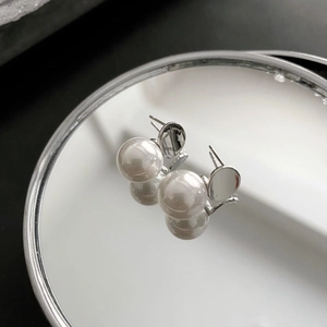Minimalist 925 silver faux pearl stud earrings with circular metal base on mirror reflection