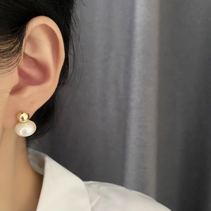 Elegant gold metal sphere and white pearl drop earrings worn by a model on white shirt