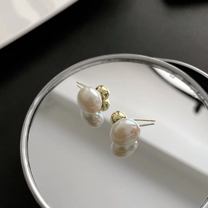 Elegant gold metal stud earrings with round white pearls on a reflective surface
