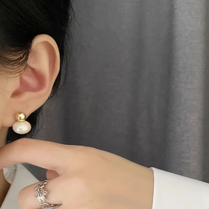 Elegant gold pearl stud earrings and nature-inspired silver ring worn by a model