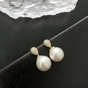 Elegant gold pearl drop earrings with sparkling zircon stones on a dark background