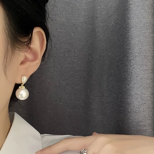 Elegant gold pearl earrings with sparkling zircon stones worn by a model in a close-up view