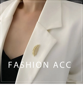 Detailed view of a gold feather brooch with micro-pave zircons on a white suit lapel