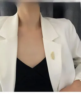 Detailed view of a gold leaf brooch with pavé zircon stones on a white blazer lapel