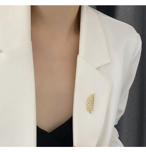Detailed close-up of a golden feather brooch with pavé zircon pinned to a white blazer