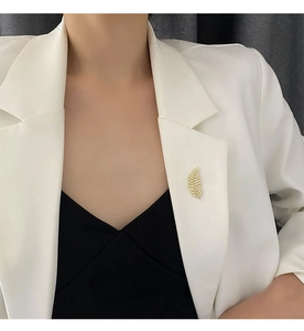 Close-up of golden feather brooch with micro-pave zircons on a white blazer