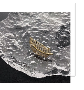 Close-up of gold feather brooch with micro-pave cubic zirconia on glass tray
