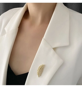 Macro detail of a gold feather brooch featuring sparkling pavé cubic zirconia on a white suit