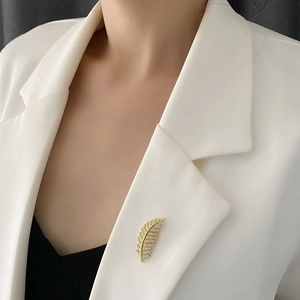 Elegant gold feather brooch with micro-pave cubic zirconia on white blazer lapel