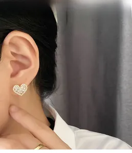 Close-up of elegant gold heart earrings with pavé crystals on woman's earlobe