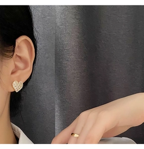 Close-up of pearl heart earring with crystals and minimalist gold ring on a model