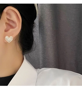 Close-up of heart-shaped pearl earrings with crystal inlay on model's ear