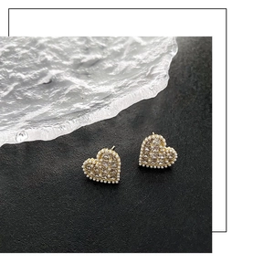 Detail of gold heart earrings with white pearls and sparkling zircon on black stone
