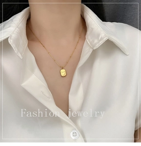 Detail of golden smile face necklace on model with minimalist rectangular pendant