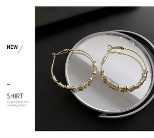 Detailed view of large golden bamboo style hoop earrings on a reflective mirror surface