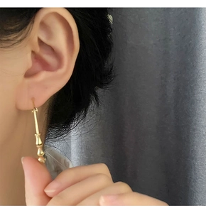 Close-up of a model wearing large golden bamboo-style hoop earrings with metallic finish