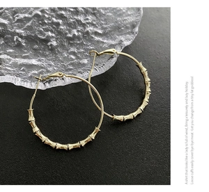 Macro detail of large golden bamboo-style hoop earrings on a dark textured background