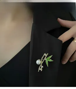 Detail of bamboo brooch with green enamel leaves and white pearl on black blazer lapel