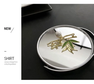 Detailed view of bamboo brooch with green enamel leaves, white pearl, and gold finish