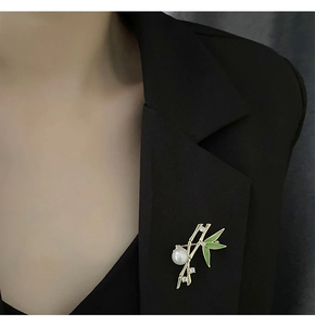 Detailed close-up of a bamboo brooch with green enamel and pearls on a black blazer lapel