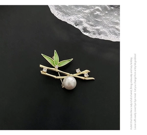 Macro detail of elegant bamboo brooch with green enamel leaves and white pearl on black background