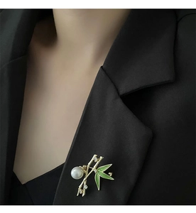 Close-up of a bamboo brooch with green enamel and a pearl on a black suit blazer
