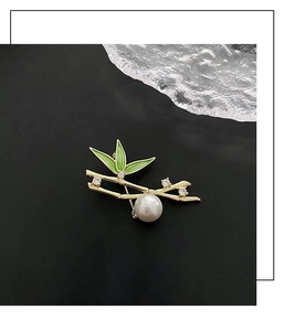 Close-up of bamboo brooch with green enamel leaves, clear crystals, and a large white pearl