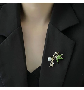 Detailed bamboo brooch with green enamel leaves and large white pearl on a black blazer