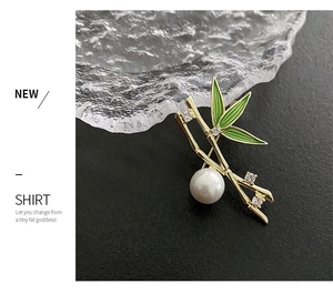 Detailed view of bamboo brooch with green enamel leaves, white pearl, and zircon stones