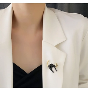 Detail view of a black and gold cat brooch pinned on a white blazer for styling