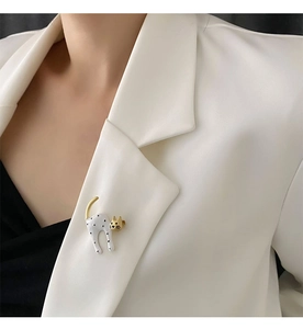 Close-up of a white polka dot cat brooch with gold accents on a white suit lapel