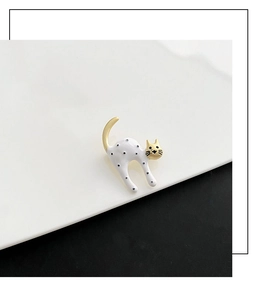 Close-up of a white and gold cat brooch with black polka dots on a ceramic plate