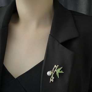 Bamboo style gold brooch with green enamel leaves and large white pearl on black suit jacket