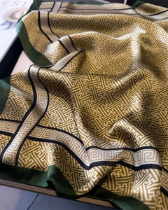 Close-up of silk scarf with gold geometric patterns and emerald green borders on tray