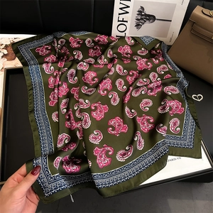 Detail of dark green paisley silk scarf with pink patterns on a luxury black tray