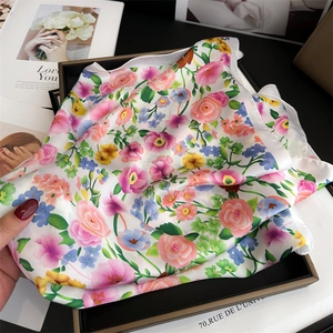 Nahaufnahme eines floralen Seidenschals mit rosa Rosen und blauen Blumen in einer Box