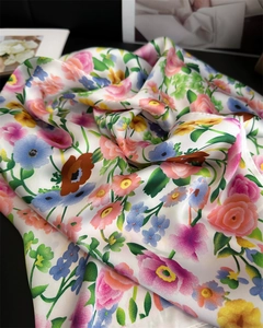 Nahaufnahme eines floralen Seidenschals mit rosa Rosen und blauen Gänseblümchen auf Weiß