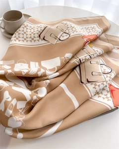 Detail of elegant printed silk scarf with houndstooth and bag patterns on a white table