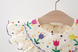 Dettaglio del ricamo a tulipano e del motivo a pois colorati sulla maglia in cotone