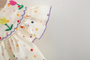 Dettaglio del vestito da neonata con pois colorati e ricami floreali di tulipani pregiati