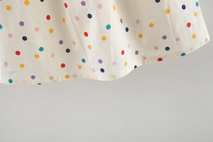 Dettaglio di pois colorati e cuciture sottili su un vestito estivo bianco da bambina
