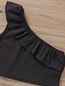 Dettaglio del top nero monospalla per bambine in maglia a costine con bordo a volant
