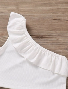 Dettaglio del top bianco a coste monospalla per bambina con scollo a balze su legno