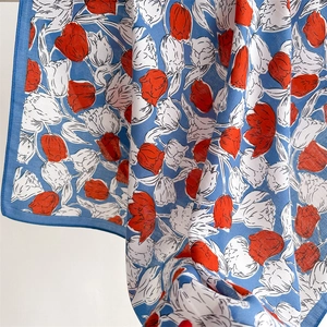 Close-up of sky blue silk scarf featuring red tulip patterns and soft fabric textures