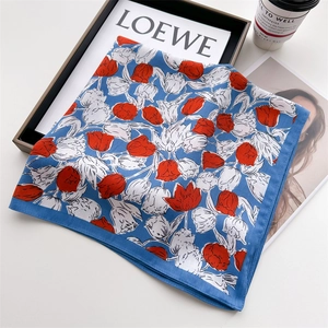 Detailed view of blue silk scarf featuring red tulip prints and delicate hemmed edges