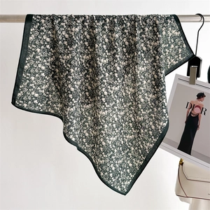 Detail of elegant floral silk scarf draped on a rack with dark green borders and pattern