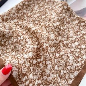 Detailed close-up of brown floral silk scarf showing fine texture and hemmed edges