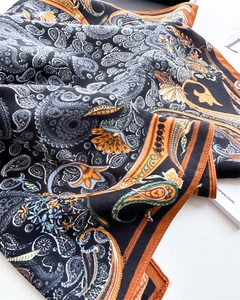 Detail of luxury paisley silk scarf with orange borders and glossy texture flat lay