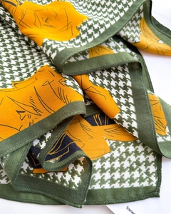 Detailed close-up of green houndstooth silk scarf with yellow floral prints and sewn edges