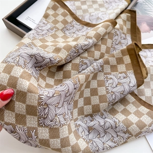 Detail of a brown houndstooth silk scarf with elegant scroll patterns and rolled edges